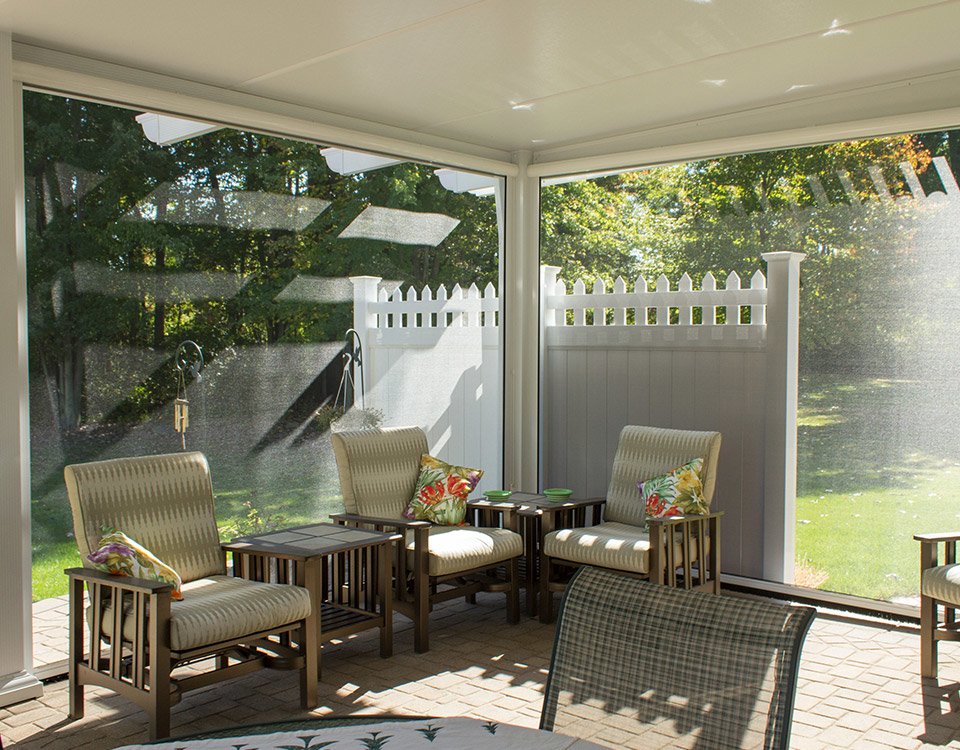 A Glass Walled Sun Room With White Cushions on Chairs
